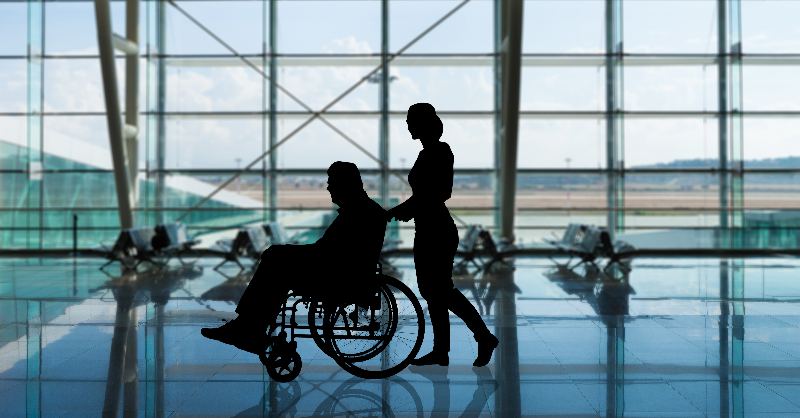 Image of a man in a wheelchair being pushed through an airport by a woman