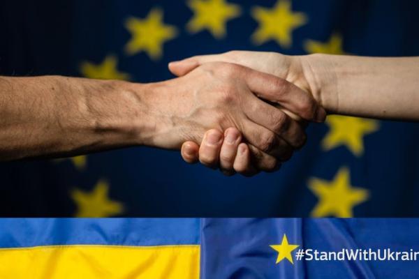 Two hands shaking across background of EU and Ukraine flags