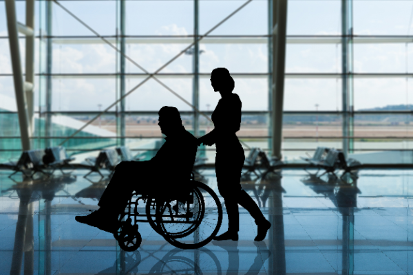 Image of a man in a wheelchair being pushed through an airport by a woman