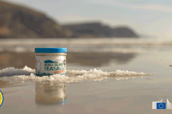 Image showing a tub of Achill Island sea salt against the background of an Achill Island beach and featuring the Protected Geographical indication and EU logos
